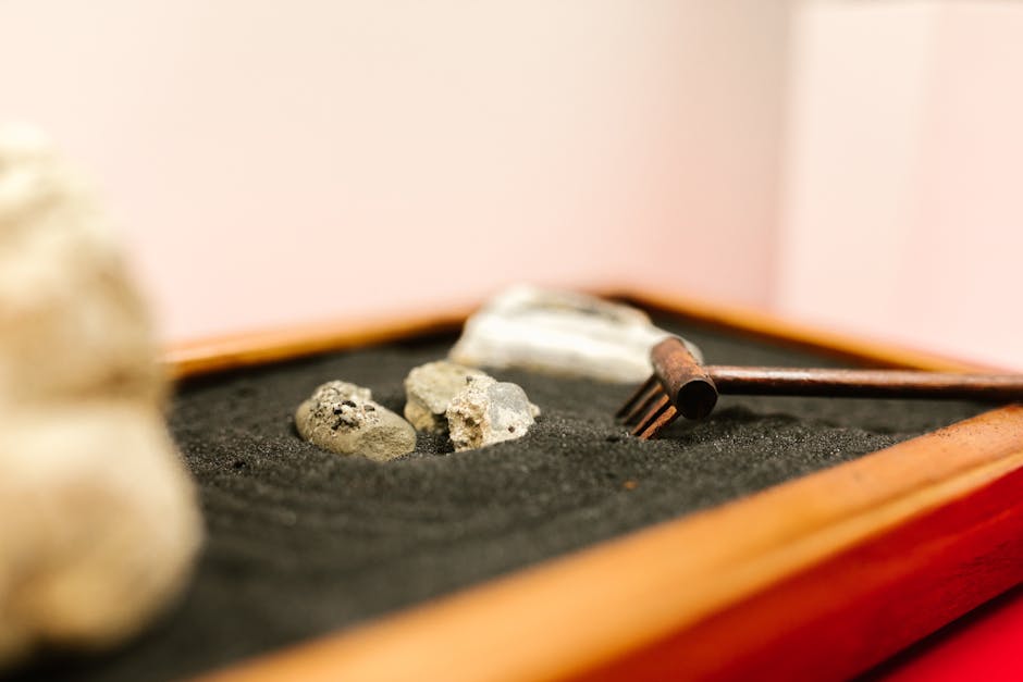 Serene close-up of miniature Zen garden with stones and small rake on black sand.